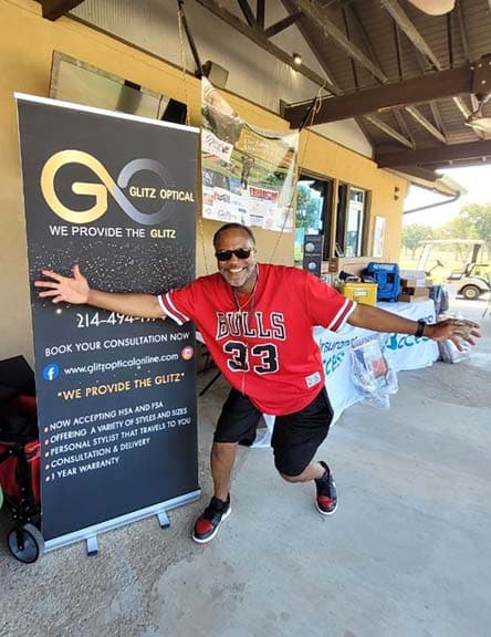 A guest celebrates beside the Glitz Optical sponsor banner
